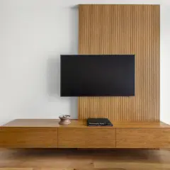 Nowoczesny salon z telewizorem na ścianie. Drewniana zabudowa i szafka RTV skutecznie ukrywają kable, tworząc minimalistyczny wygląd.