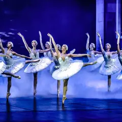 Grupa tancerek baletowych w białych tutu na niebieskiej scenie z mgłą.
