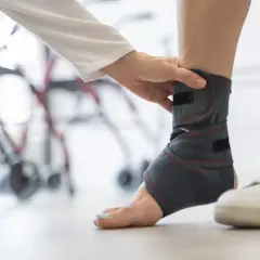 Una mano applica un tutore ortopedico alla caviglia per supporto e stabilità, aiutando a recuperare da un infortunio.