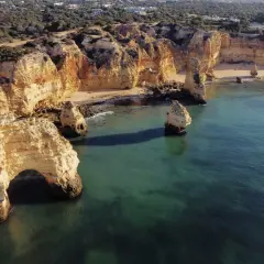 Skaliste klify Algarve, z łukiem skalnym i samotnymi formacjami, wpadają do turkusowego morza. Widok przypomina o urokach wybrzeża, jakbyśmy byli w pobliżu Faro Lizbona.