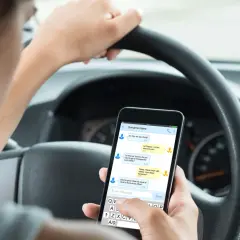 Person håller en telefon i bilen och skriver ett meddelande.