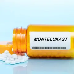 Pomarańczowa butelka leku z etykietą MONTELUKAST, z której wysypały się białe tabletki.