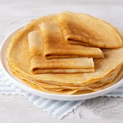 Pile de crêpes dorées, certaines pliées, sur une assiette blanche. Un délice sans oeuf pour un petit-déjeuner léger.