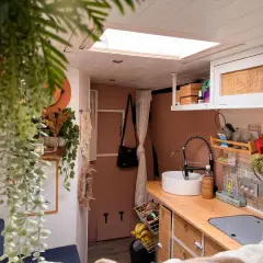 Intérieur de fourgon aménagé : cuisine avec évier, robinet, placards et plantes.
