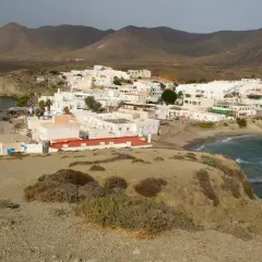 Vista panorámica de la playa Isleta del Moro, con casas blancas, mar azul y montañas áridas al fondo.