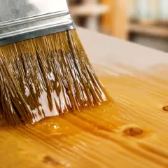 Un pinceau applique du vernis sur du bois. La question "peut on peindre sur du vernis" se pose pour ce projet de finition.