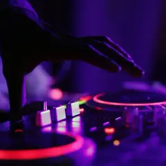 Dłoń DJ-a nad konsolą, czerwone i fioletowe światła. Czy to ZAIKS co to za muzyka?