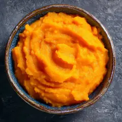 Un cuenco de cremoso puré de boniato, con su vibrante color naranja, listo para ser disfrutado.