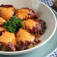 Pimientos rellenos de carne, cubiertos con una cremosa salsa naranja y adornados con perejil fresco.