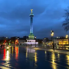 Wieczorny Paryż po deszczu. Kolumna Bastylii lśni w świetle latarni, a mokry asfalt odbija światła miasta.