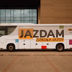Biały autobus szkolny z napisem "JAZDAM SZKOŁA JAZDY" i numerem telefonu.