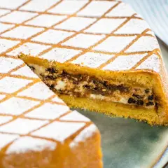 Una fetta di cassata al forno, con la sua copertura a rombi di zucchero a velo, rivela un ripieno goloso di ricotta e cioccolato.