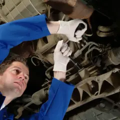 Mechanik w białych rękawiczkach dokręca śrubę pod samochodem. Może to być związane z objawami wybitych tulei tylnej belki.