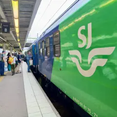 Folk väntar på tåget vid perrong B. En grön SJ-tågvagn syns tydligt. Kanske är det början på en resa till England från Sverige.