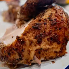 Un morceau de poulet au four cuisson lente, doré et savoureux, servi sur une assiette blanche.