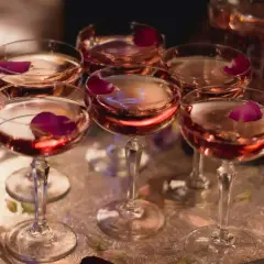 Eleganckie kieliszki z różowym winem, ozdobione płatkami róży, czekają na degustację. W tle widać karafkę z tym samym trunkiem, być może to wykwintny tokaji aszu.