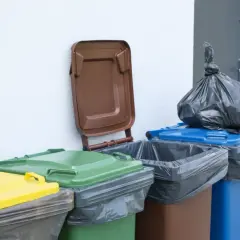 Kolorowe pojemniki na śmieci stoją przy ścianie. Zastanawiasz się, gdzie wyrzucić pościel? Sprawdź oznaczenia na koszach.