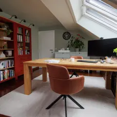 Accogliente angolo studio in mansarda con scrivania in legno, librerie rosse e lucernario.