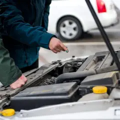 Två personer gör en bil kontroll vid en öppen motorhuv. En pekar på något i motorn.