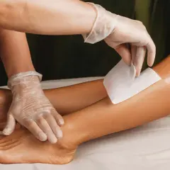 Una mano guantata applica una striscia di cera su una gamba. Per una ceretta efficace, i peli devono essere lunghi circa mezzo centimetro.