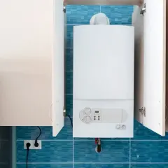 Une chaudière blanche est installée dans un coffrage mural, avec des portes ouvertes révélant le fond carrelé de bleu.