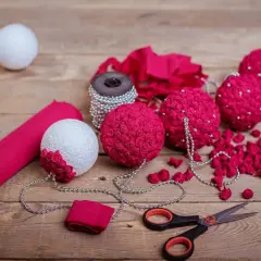 Jak ozdobić bombkę ze styropianu? Na drewnianym stole leżą białe i różowe bombki, nożyczki, koraliki i różowa bibuła.