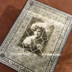 Stare zdjęcie kobiety z fryzurą w stylu retro, pęknięte i umieszczone na ozdobnej powierzchni.