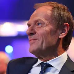 Uśmiechnięty mężczyzna w garniturze, z lekko przerzedzonymi włosami. Czy Tusk jest rudy? Jego włosy mają odcień jasnego brązu.