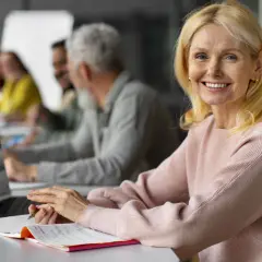 Uśmiechnięta kobieta z pokolenia X, od kiedy zaczęła naukę, pracuje przy laptopie w sali szkoleniowej.