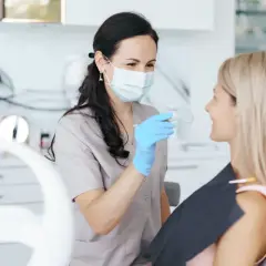 Dentystka bada uśmiech pacjentki. Może to być kontrola po uderzeniu, gdy ruszający się ząb mleczny u dziecka wymaga uwagi.