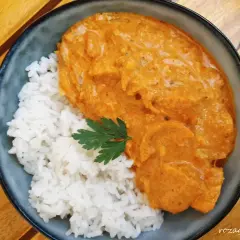 Aksamitny butter chicken w kremowym sosie, podany z ryżem i listkiem pietruszki. Pyszne danie na drewnianym stole.