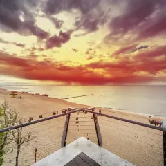 Spektakularny zachód słońca nad morzem, z ognistymi chmurami i łodziami na piaszczystej plaży. Pogorzelica w całej okazałości.