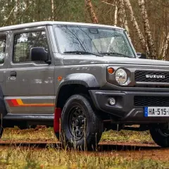 Szary Suzuki Jimny 2026 z kolorowymi pasami na boku, gotowy na terenową przygodę w lesie.