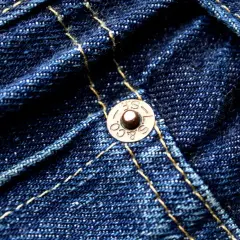 Close-up of dark blue denim with yellow stitching. A copper rivet, marked "S.F. & CO. L.S.", is visible, a testament to the durability of these jeans.