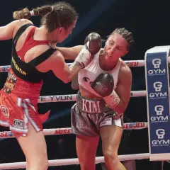 Two female boxers in a strawweight boxing match exchange punches in the ring. One boxer lands a blow to the other's face.