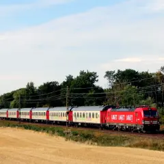Röd lokomotiv drar en lång tågvagn genom ett fält med gulnande säd. En nattåg Stockholm Berlin på väg.