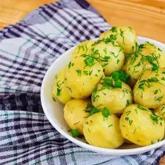 Młode ziemniaki w misce, posypane koperkiem i szczypiorkiem. Idealne na lato, a ile gotować młode ziemniaki? Krótko!