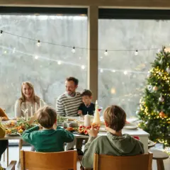 Familie feiert Weihnachten am festlich gedeckten Tisch, mit geschmücktem Baum im Hintergrund.