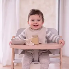 Ein lächelndes Baby sitzt im Hochstuhl, bereit für Brei. Was kann ein Baby mit 9 Monaten? Es kann schon viel, wie dieses fröhliche Kind beweist!