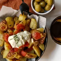 Patatas bravas con alioli, servidas con aceitunas y una bebida oscura.
