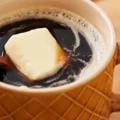 Kawa z masłem, popularna w diecie ketogenicznej, ma swoje przeciwwskazania. Na zdjęciu kostka masła w kubku kawy.