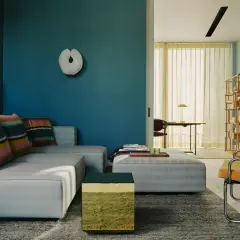 Soggiorno moderno con divano grigio, cuscini colorati e pareti blu intenso. Un tavolino cubico verde e oro aggiunge un tocco di vivacità.