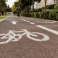 Ścieżka rowerowa z białym znakiem P23 i strzałką kierunkową. W oddali widać rowerzystę.