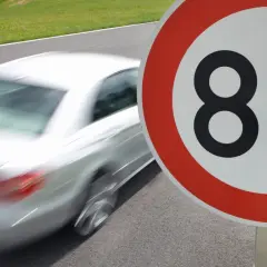 Znak ograniczenia prędkości do 80 km/h. Biały samochód pędzi po drodze, przypominając o przepisach ruchu drogowego i ograniczeniach prędkości w Polsce.