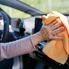 Mano limpiando el salpicadero del coche con un paño naranja. Descubre trucos caseros para limpiar el salpicadero del coche y mantenerlo impecable.