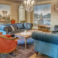 Elegancki salon w hotelu 5 gwiazdkowym. Miękkie sofy, aksamitne fotele i zabytkowy piec tworzą przytulną atmosferę.