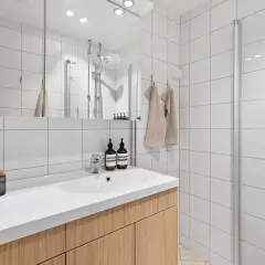 Nowoczesna łazienka z białymi płytkami, drewnianą szafką pod umywalkę i przeszkloną kabiną prysznicową. Różne rodzaje kabin prysznicowych mogą odmienić każde wnętrze.