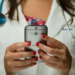 Lekarka w białym kitlu z czerwonymi paznokciami trzyma telefon. Czy pracodawca widzi kod choroby na ekranie?