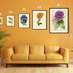 Un sofá amarillo bajo un marco din A3 con flores moradas y rosadas.