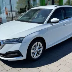 Białe, duże auto rodzinne typu kombi stoi przed salonem samochodowym. Idealne na wakacyjne wyjazdy i codzienne dojazdy.
